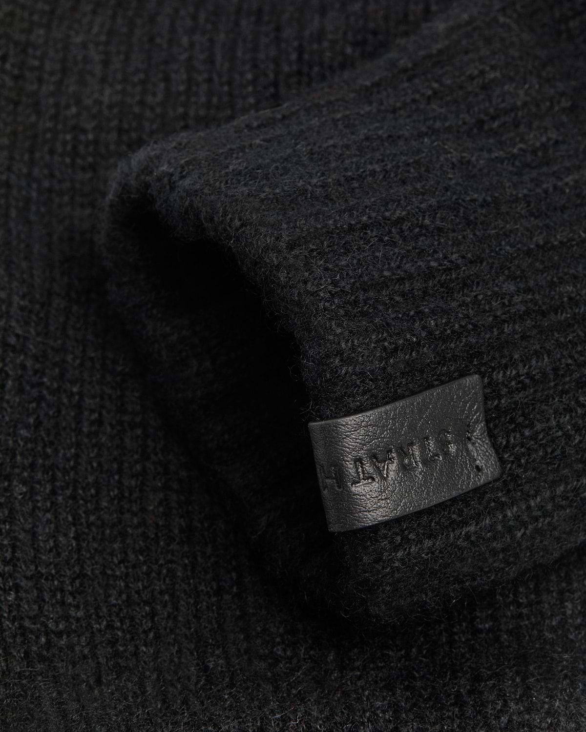 Black ribbed fingerless glove showing textured knit and leather tag
