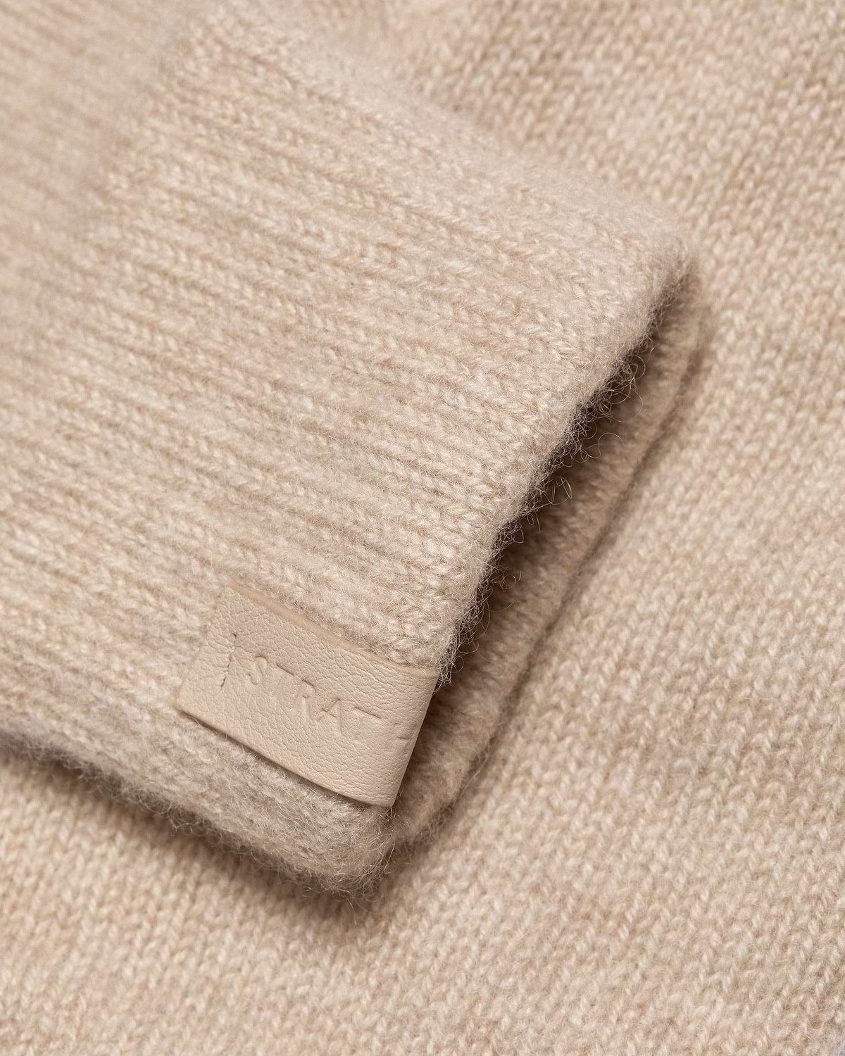 Oat-coloured fingerless cashmere glove showing knit texture and leather tag