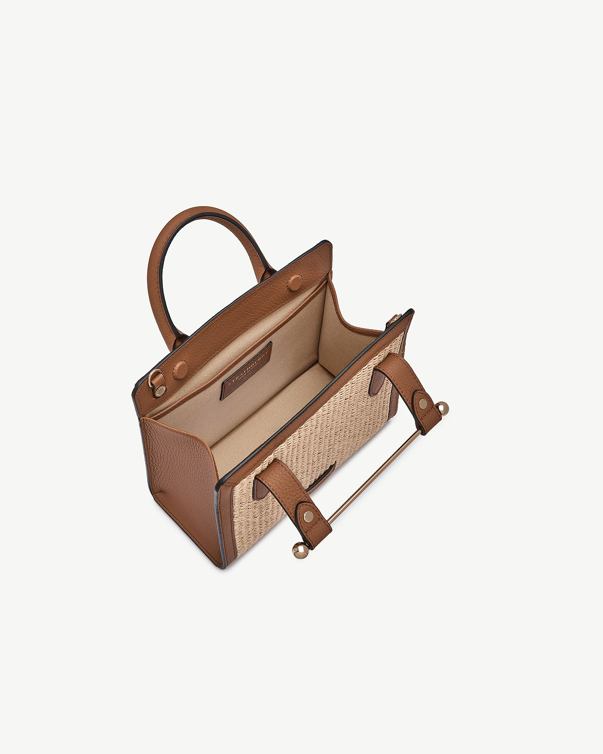 Tan leather mini tote with natural raffia panels, open top and interior pocket.