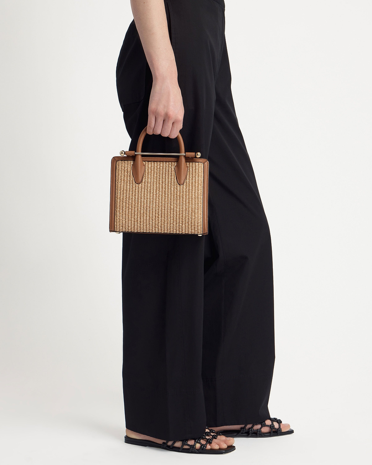 Mini tan raffia tote with leather trim and top handles held by model.