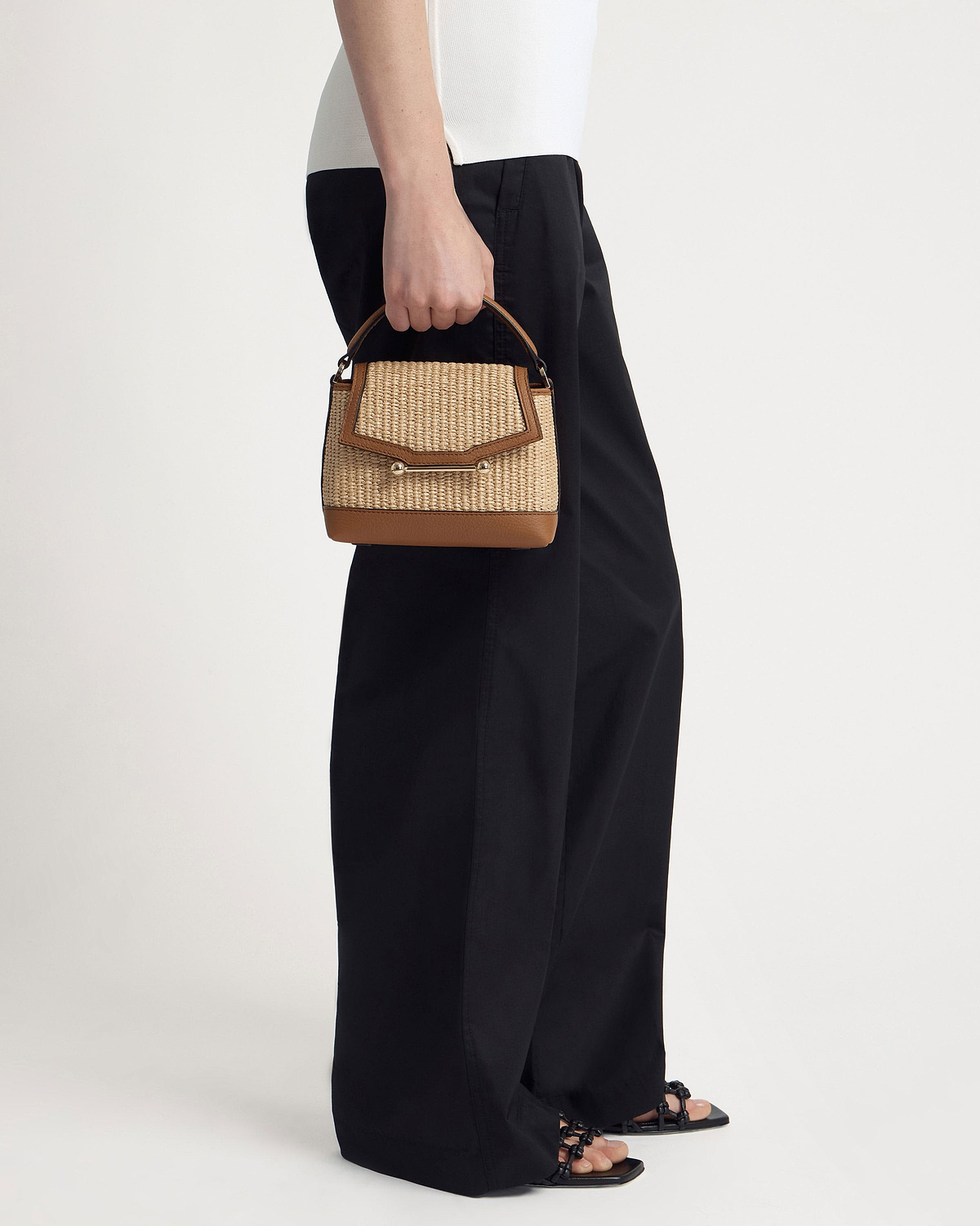 Model holding a tan and natural raffia Mosaic Nano top-handle bag.