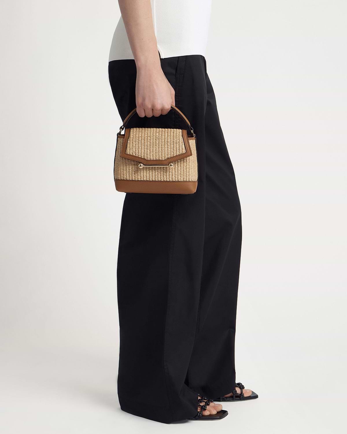 Model holding a tan and natural raffia Mosaic Nano top-handle bag.