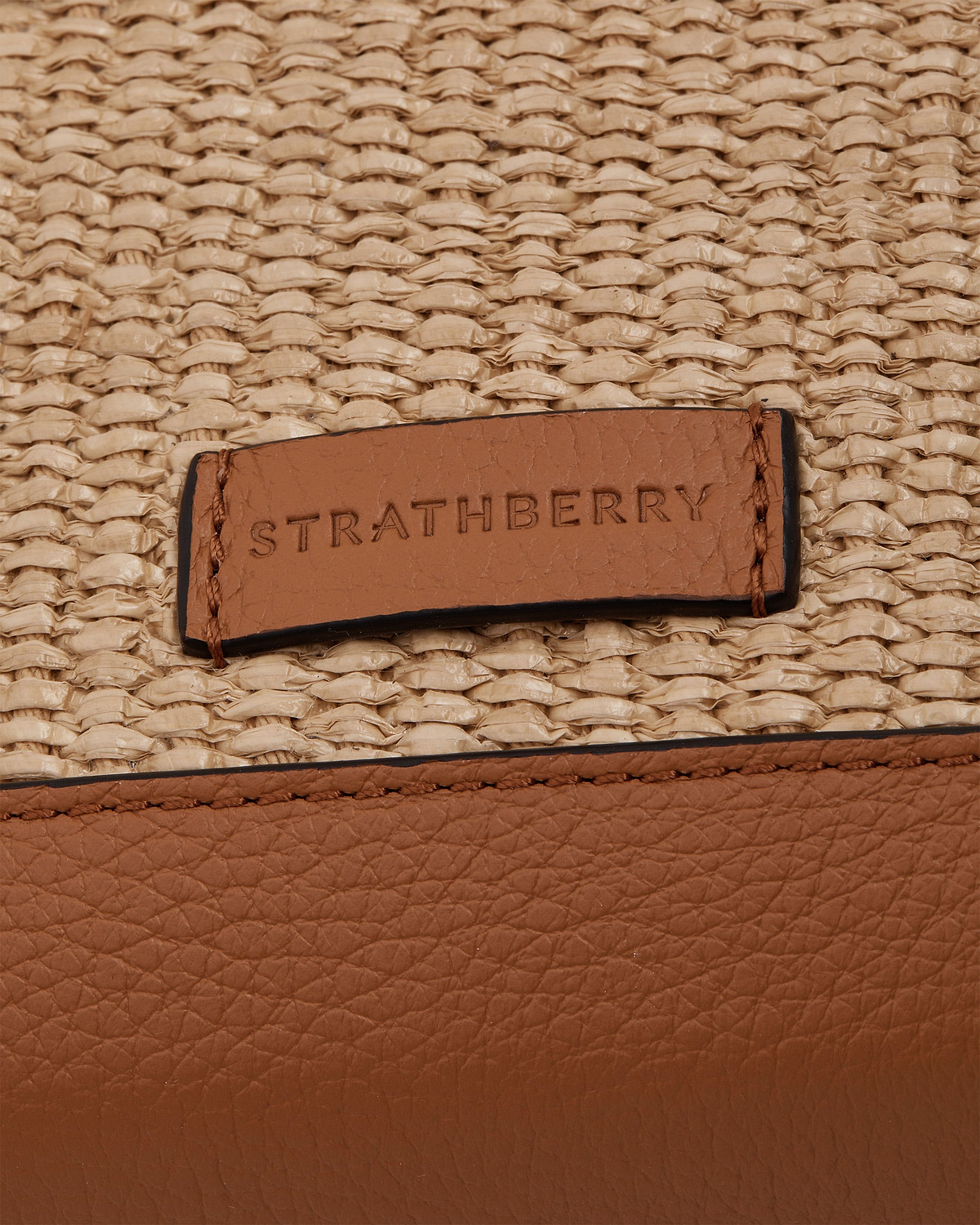 Tan leather trim and woven natural raffia with embossed STRATHBERRY logo tag.