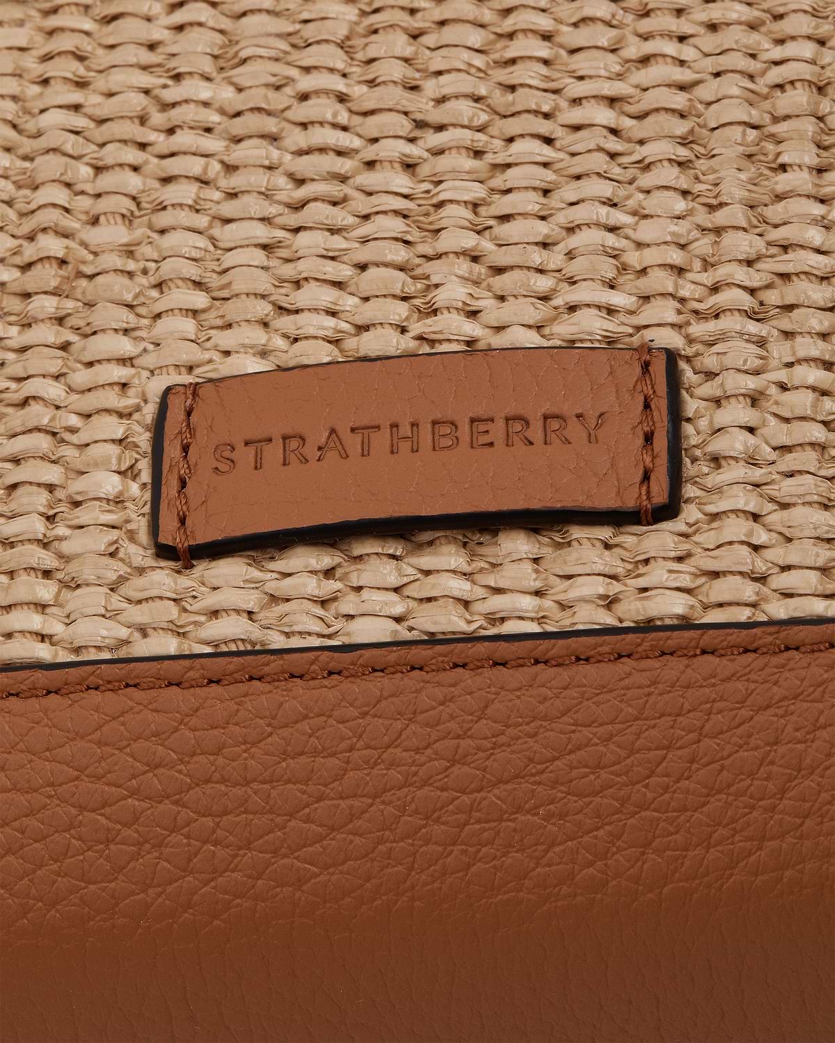 Tan leather trim and woven natural raffia with embossed STRATHBERRY logo tag.