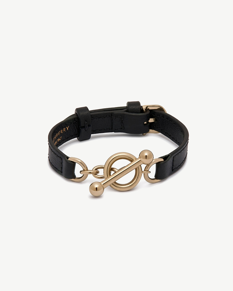 Black leather Strathberry Kite bracelet with gold circular toggle fastener.