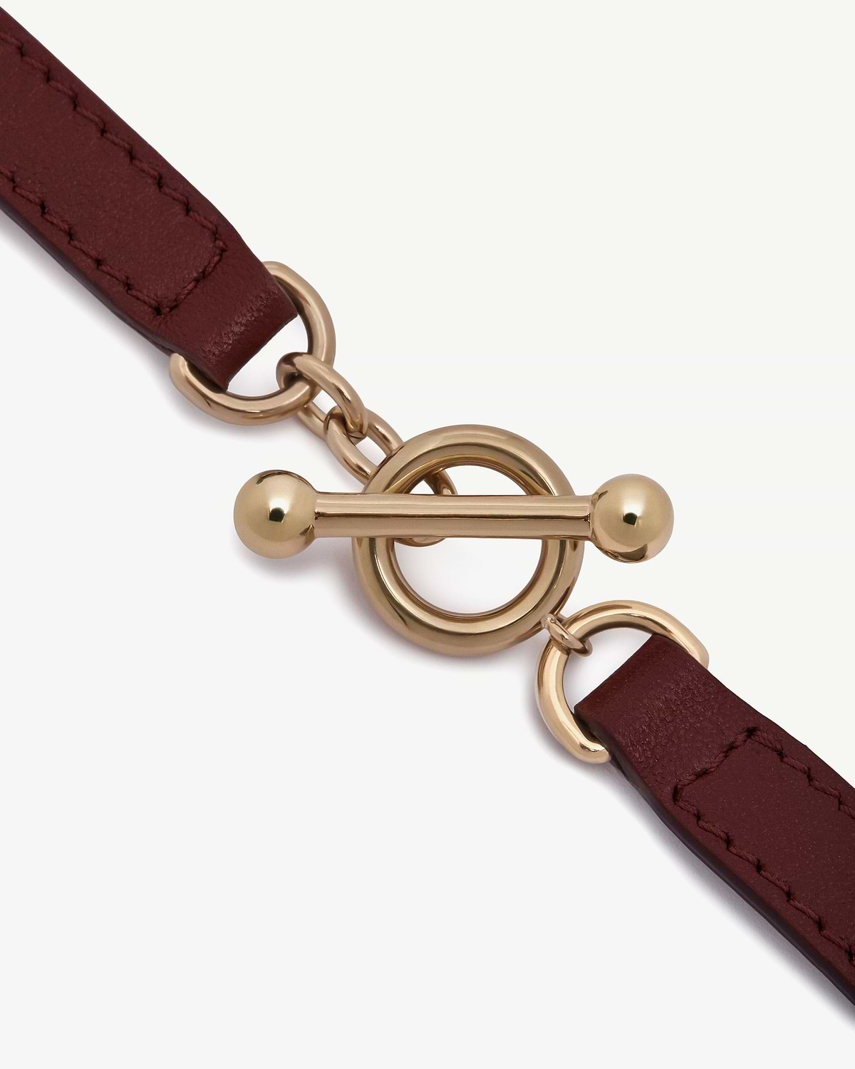 Oxblood leather bracelet with gold toggle fastening and stitched straps.