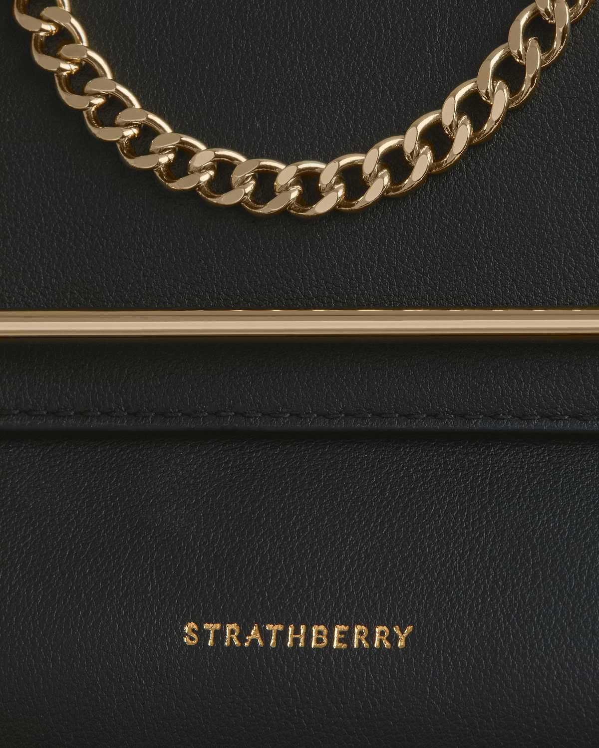 Black leather bag with gold chain, bar trim and Strathberry logo.