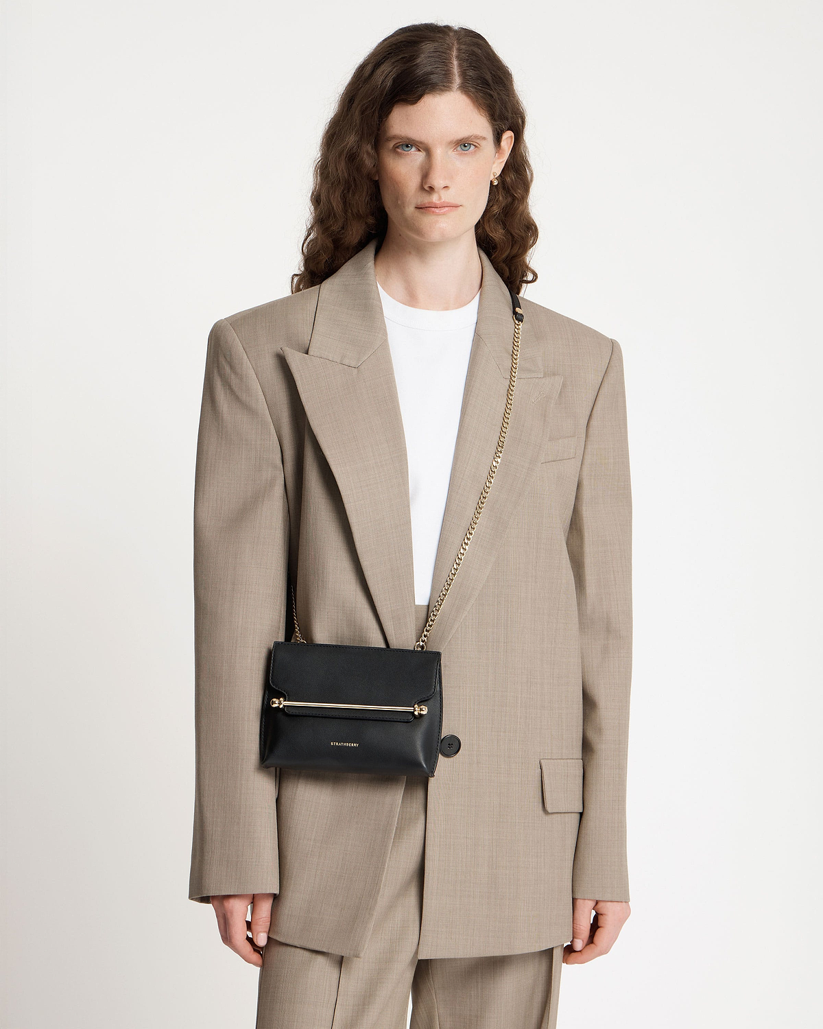 Model wearing black Strathberry Stylist Mini with gold bar detail and chain strap.