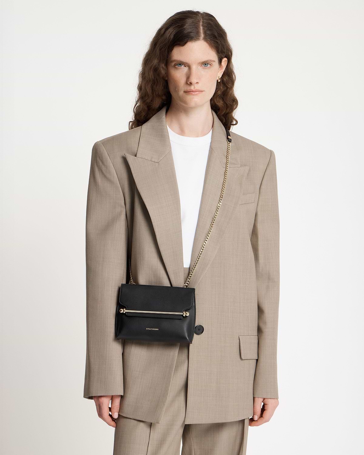 Model wearing black Strathberry Stylist Mini with gold bar detail and chain strap.