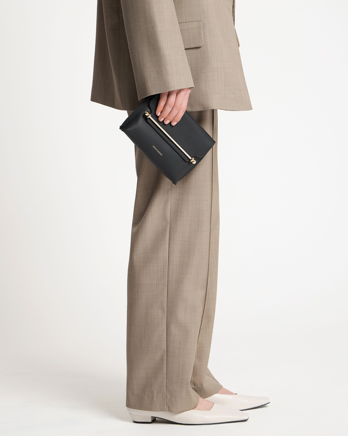 Model holding a black Strathberry Stylist Mini clutch by her side.