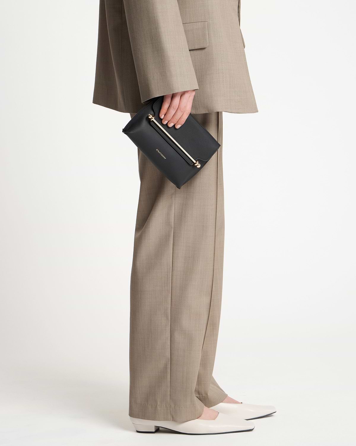 Model holding a black Strathberry Stylist Mini clutch by her side.
