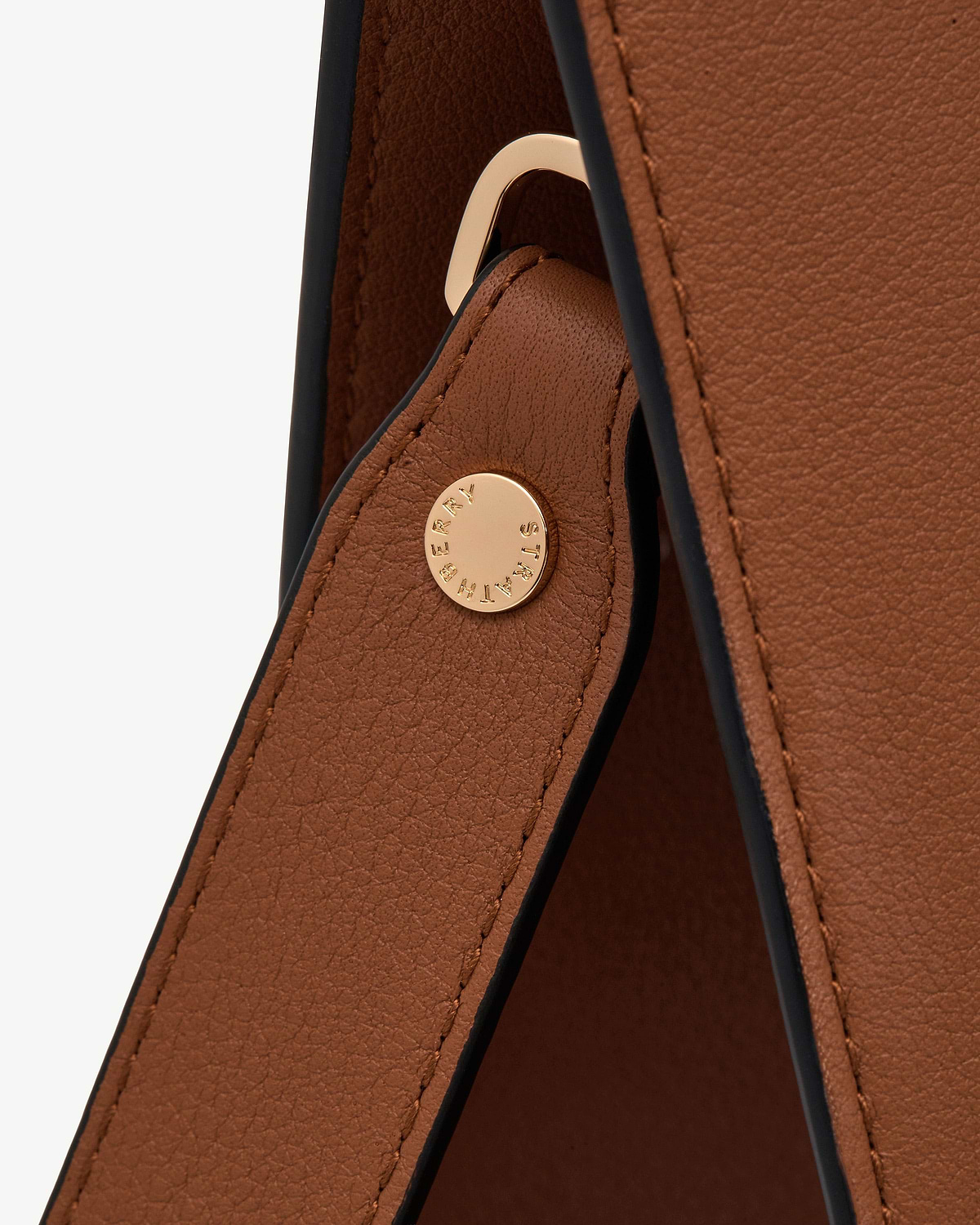 Close-up of chestnut leather tote strap with gold circular metal stud.