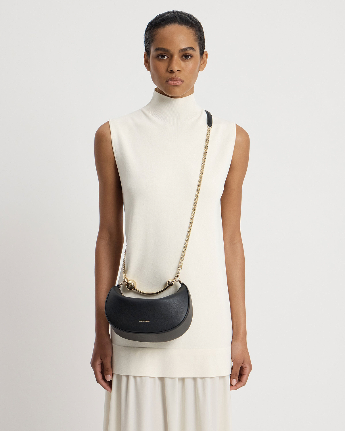 Model wearing black Strathberry Crescent Moon Mini shoulder bag with gold hardware