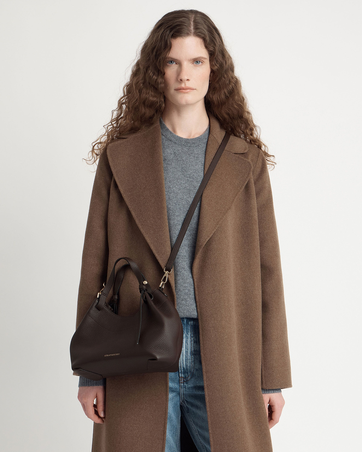 Model wearing brown coat with espresso leather Strathberry Barra Mini crossbody bag