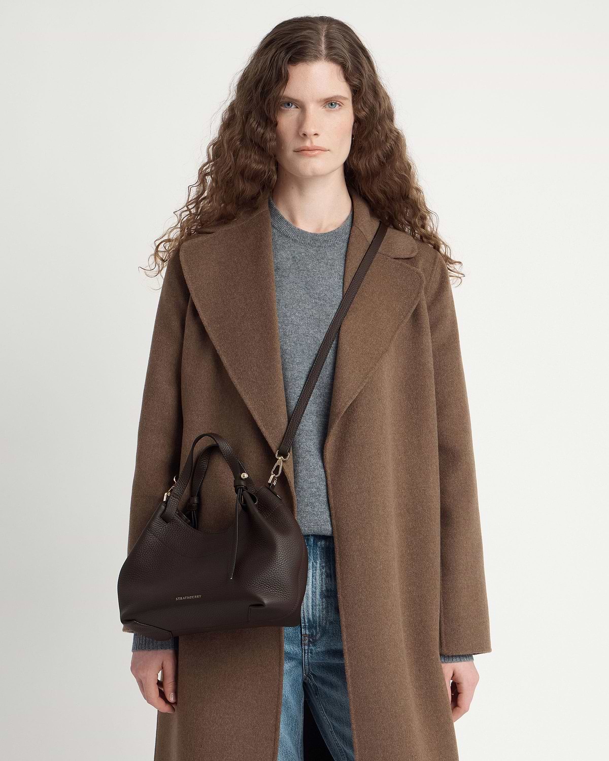 Model wearing brown coat with espresso leather Strathberry Barra Mini crossbody bag