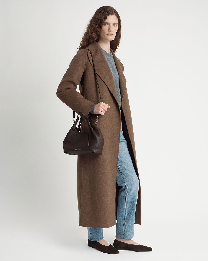 Model wearing long brown coat and jeans holding espresso leather Barra Mini bag.