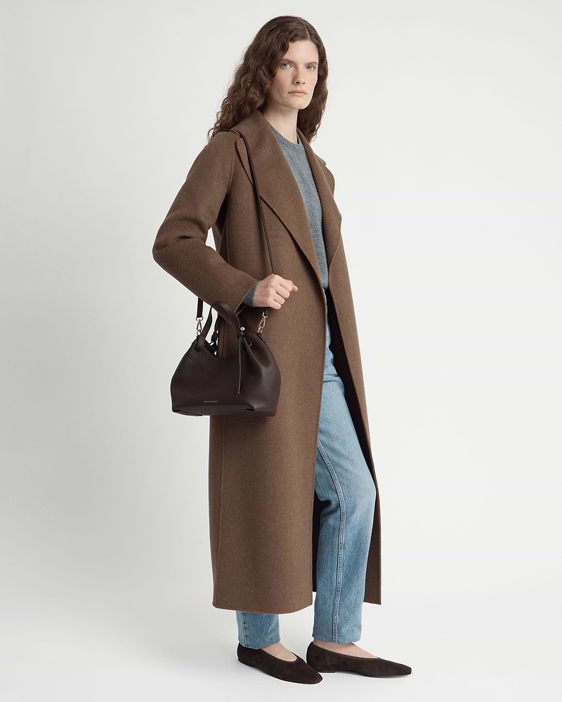 Model wearing long brown coat and jeans holding espresso leather Barra Mini bag.