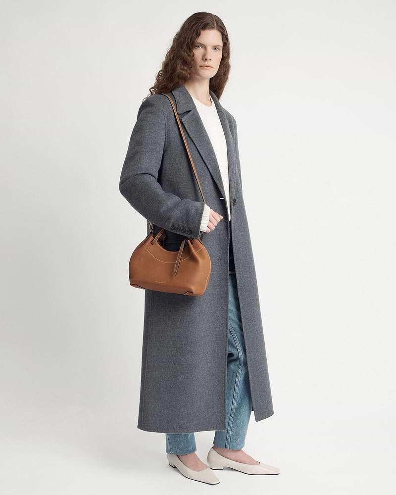 Woman in long grey coat holds tan leather shoulder bag with top handle