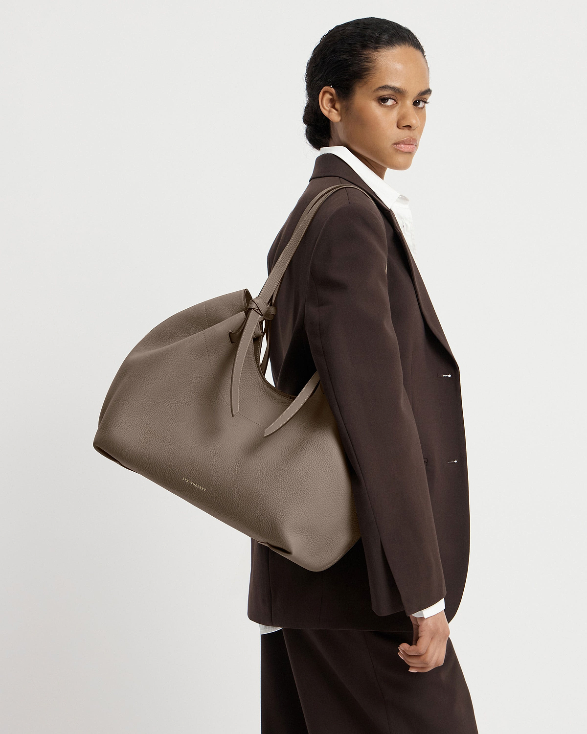 Model wearing brown blazer carrying taupe Strathberry Barra tote over shoulder
