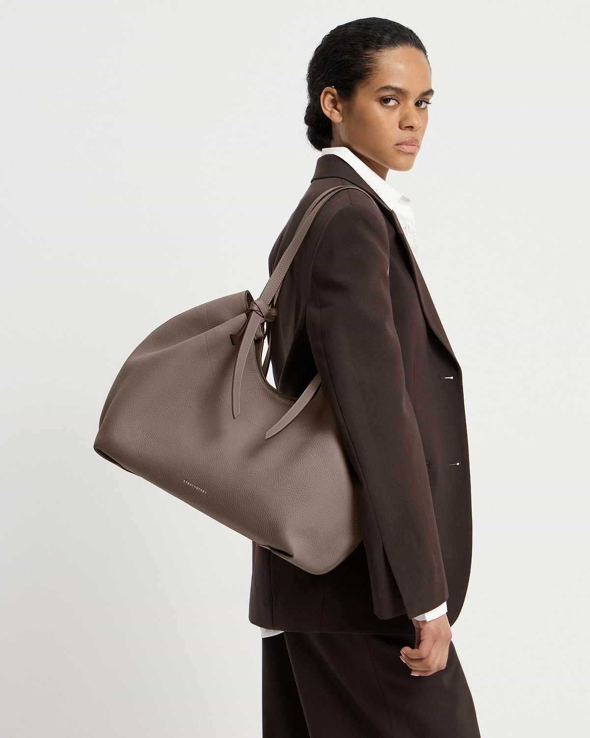 Model wearing brown blazer carrying taupe Strathberry Barra tote over shoulder
