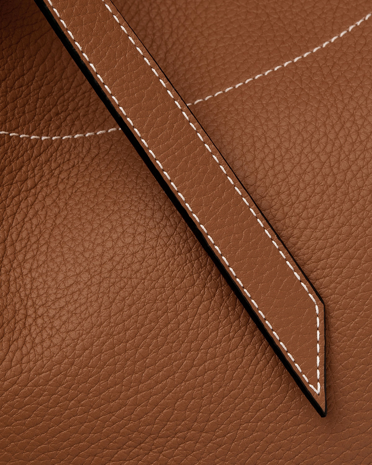 Close-up of tan pebbled leather tote showing stitched strap and seam detail.