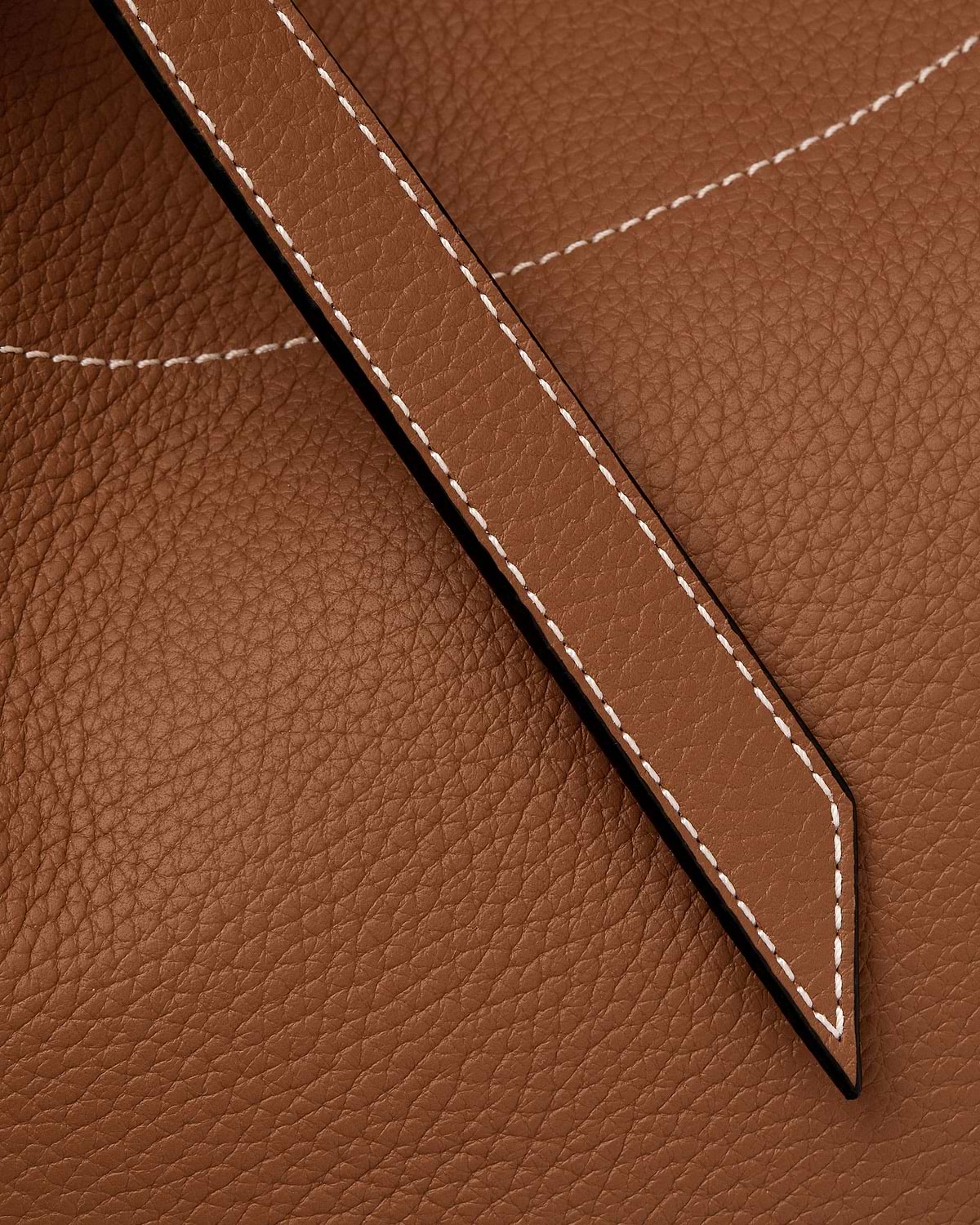Close-up of tan pebbled leather tote showing stitched strap and seam detail.