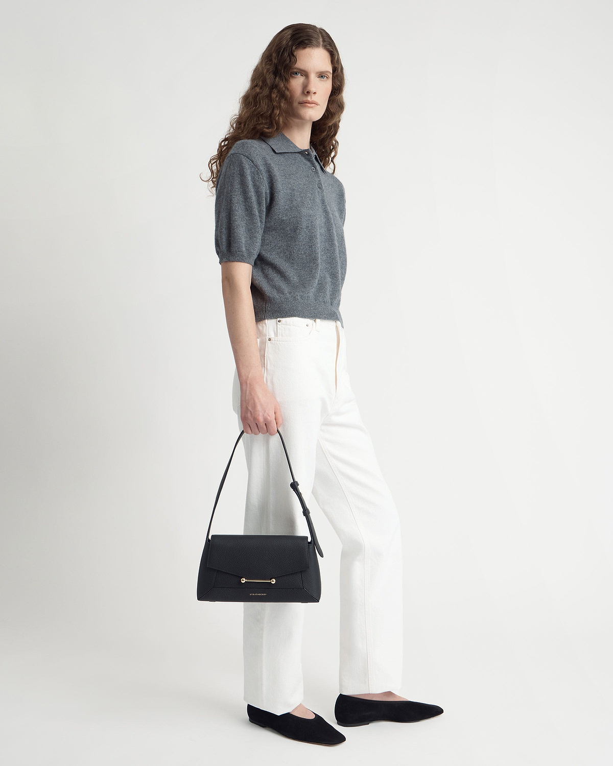 Model in grey top and white trousers holding a black Mosaic shoulder bag.