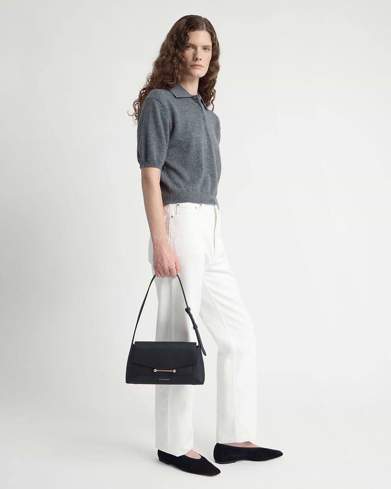 Model in grey top and white trousers holding a black Mosaic shoulder bag.