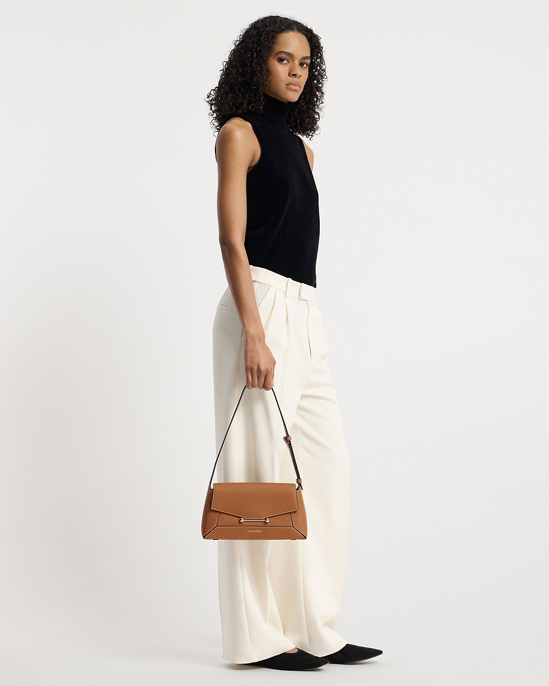 Model holding tan Strathberry Mosaic Shoulder bag by top handle.