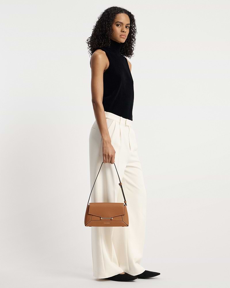 Model holding tan Strathberry Mosaic Shoulder bag by top handle.