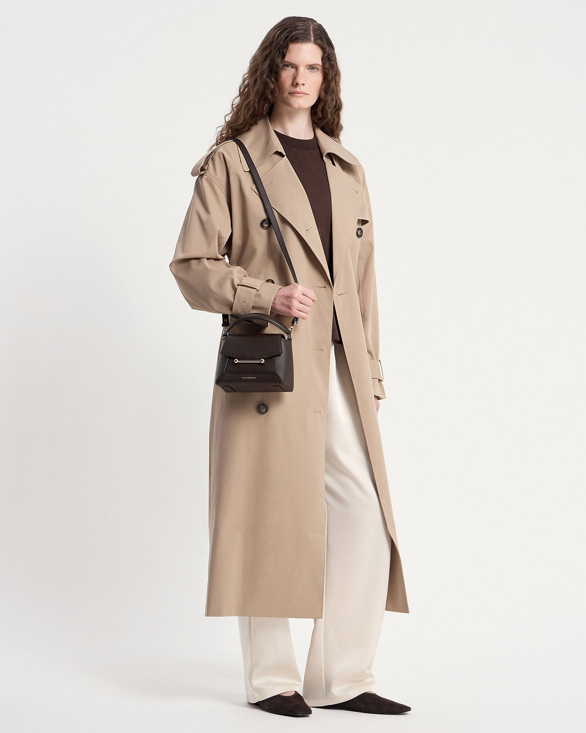 Model wearing a beige trench coat holding an espresso Mosaic Nano bag with shoulder strap.