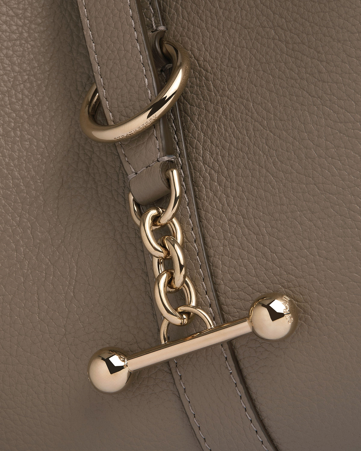 Taupe pebbled leather with gold chain hardware and engraved Strathberry metal ring.