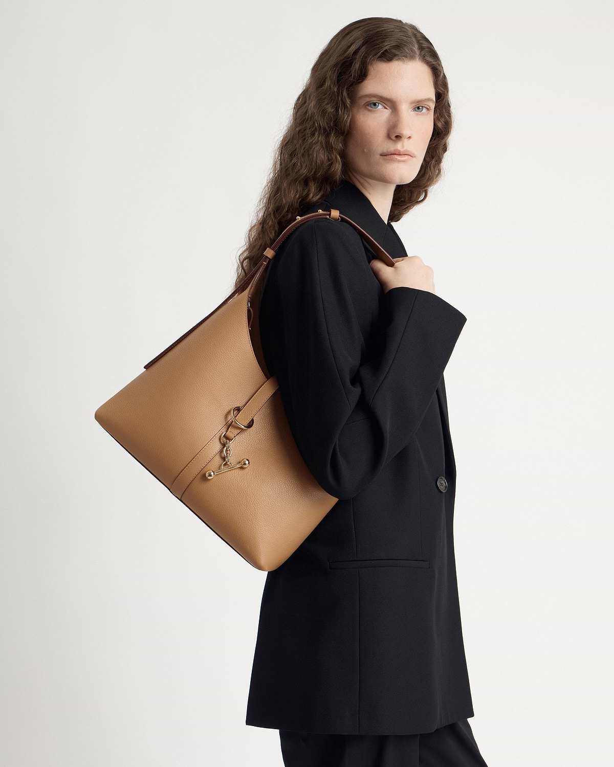 Woman in black blazer carrying caramel Kite Hobo shoulder bag over her shoulder.