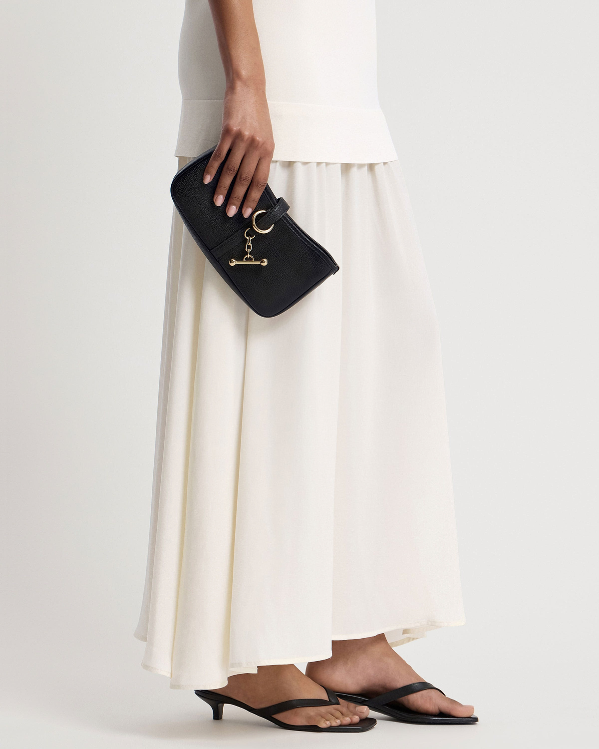 Model holding black kite on a chain bag with gold T-bar charm and pebbled leather.