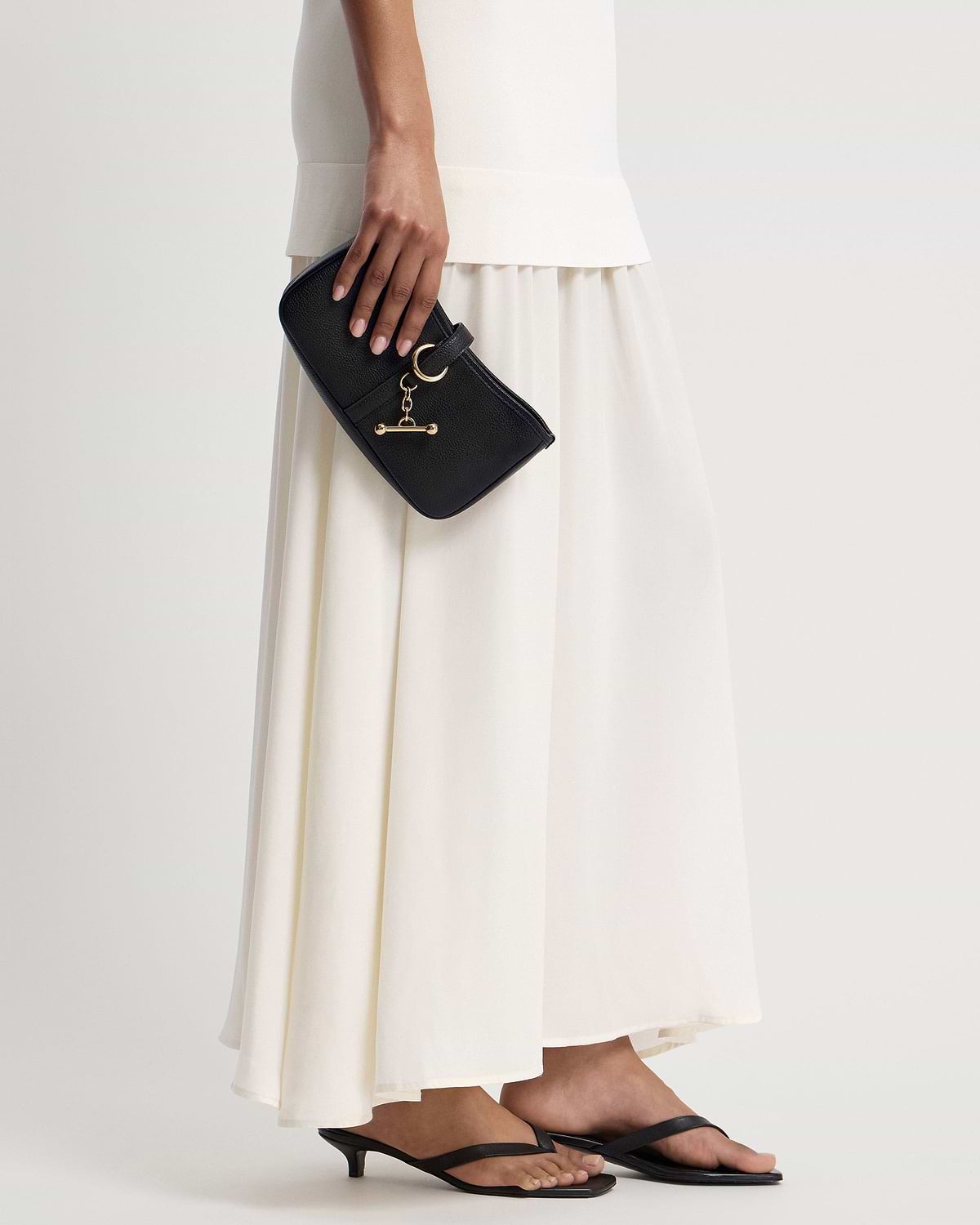 Model holding black kite on a chain bag with gold T-bar charm and pebbled leather.