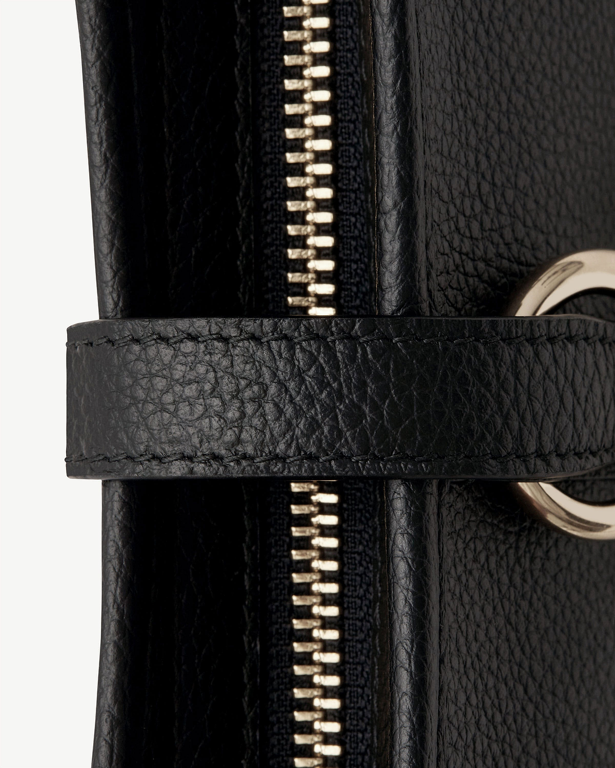 Close-up of black pebbled leather bag zipper, strap and gold metal ring.