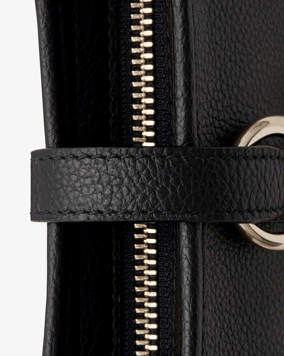 Close-up of black pebbled leather bag zipper, strap and gold metal ring.
