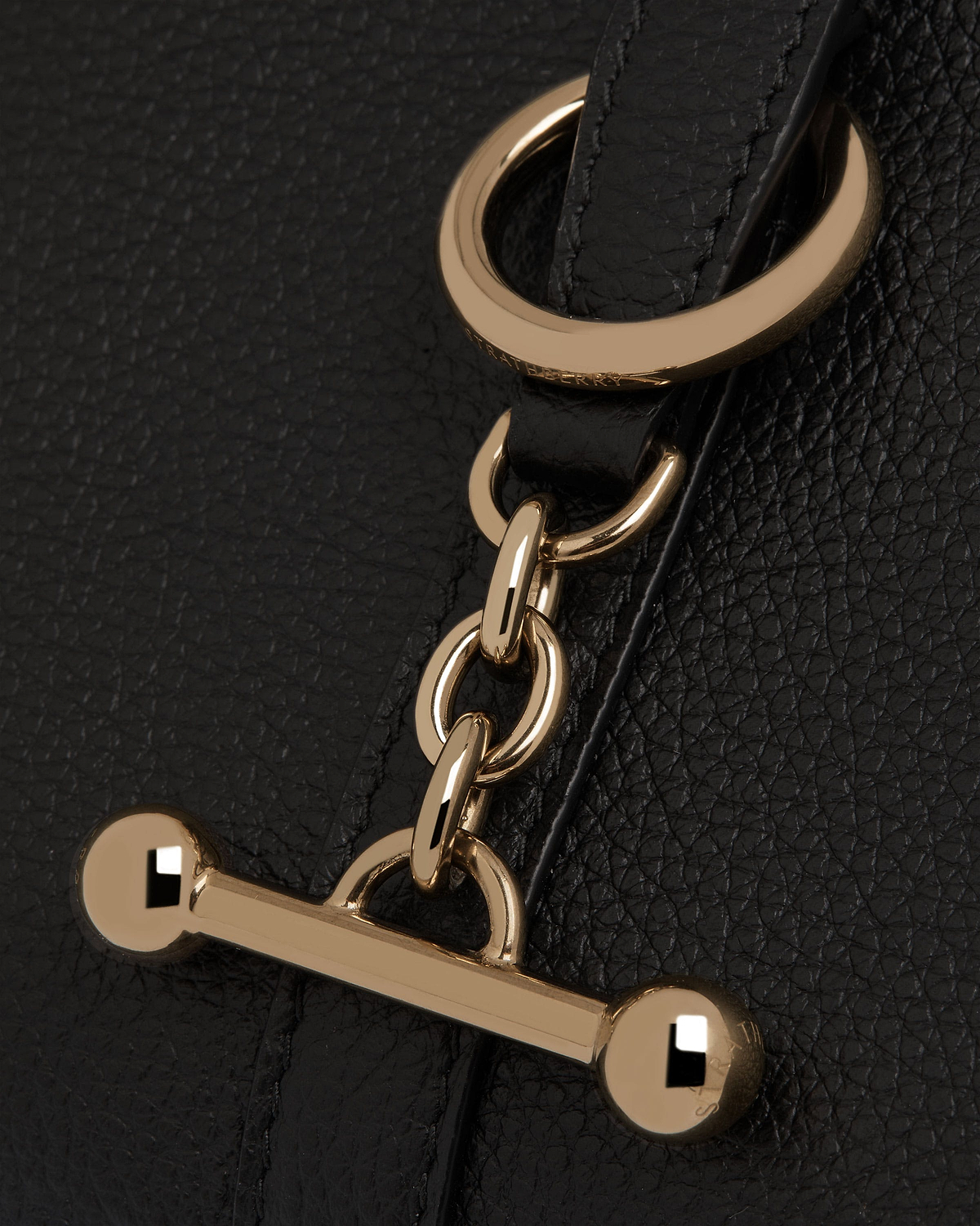 Black pebbled leather close-up of Strathberry gold chain and bar toggle hardware.