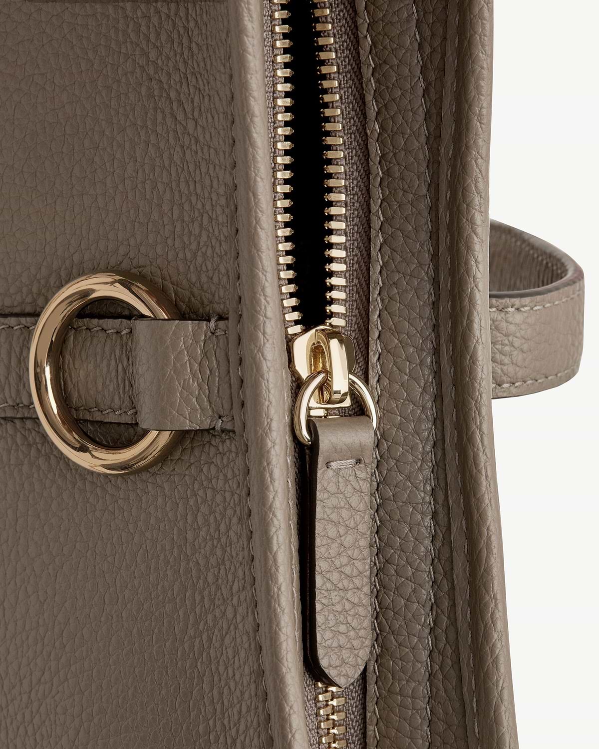 Close-up of taupe pebbled leather handbag zip and gold ring hardware.