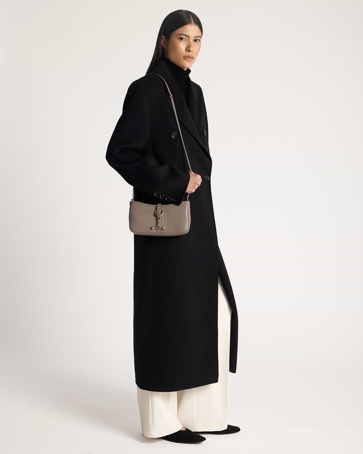 Woman in black coat carrying a taupe leather shoulder bag with chain strap