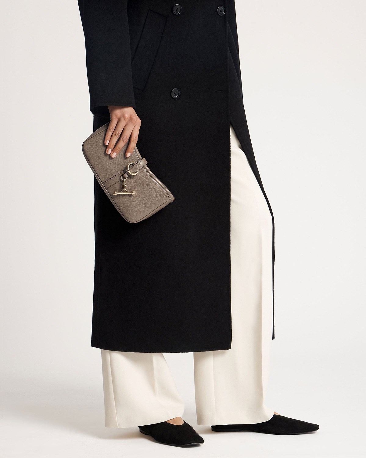 Hand holding taupe Kite on a Chain clutch with gold hardware and black coat.