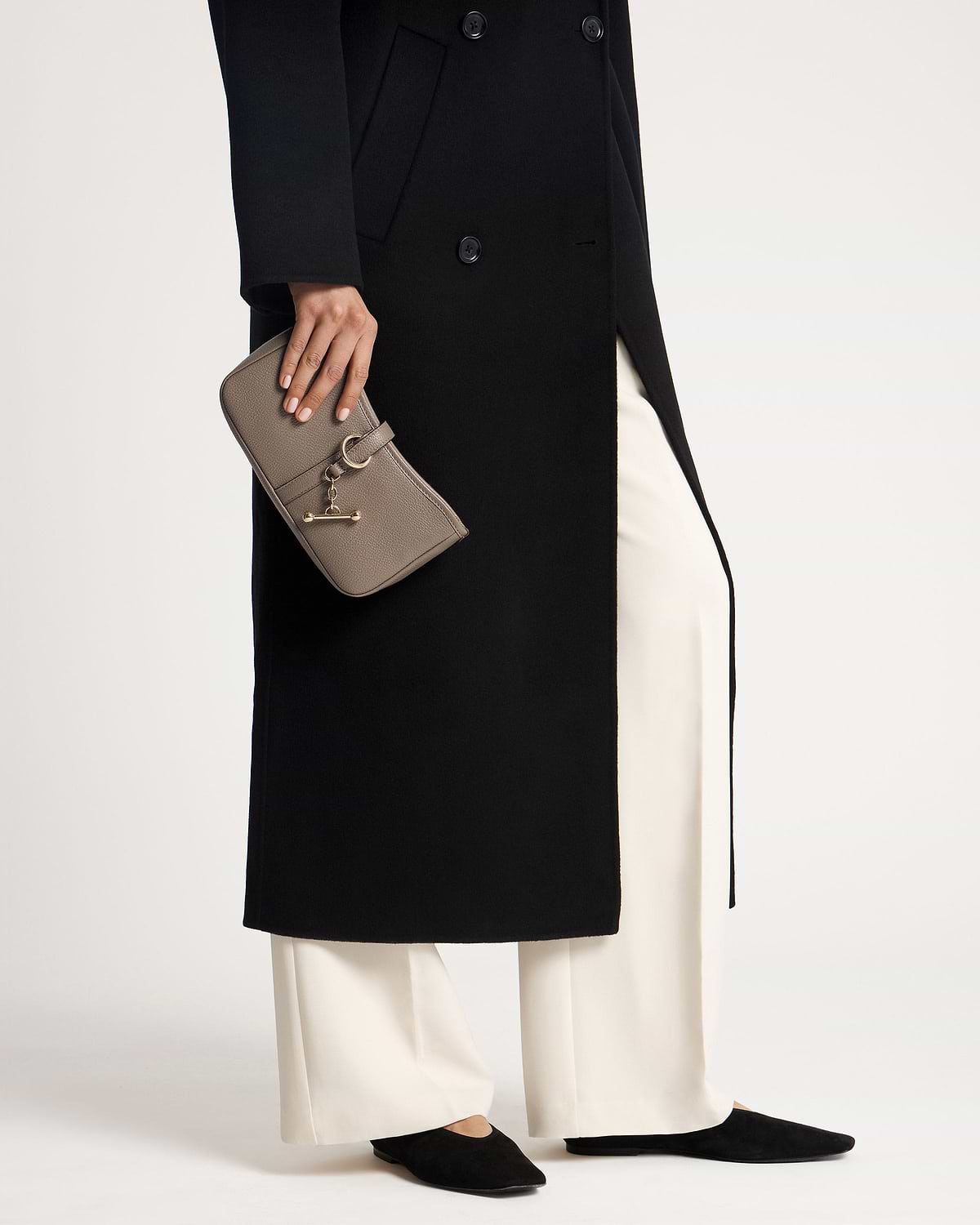Hand holding taupe Kite on a Chain clutch with gold hardware and black coat.