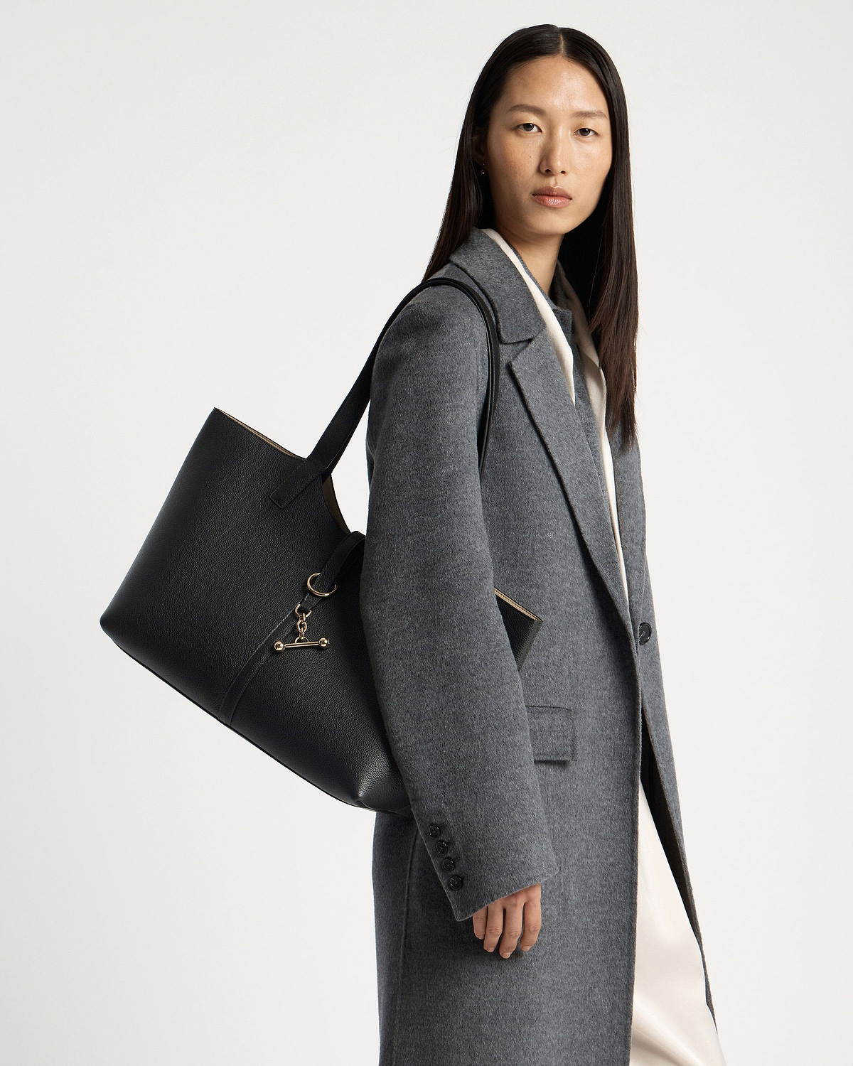 Model wearing a grey coat carrying a black kite tote shoulder bag