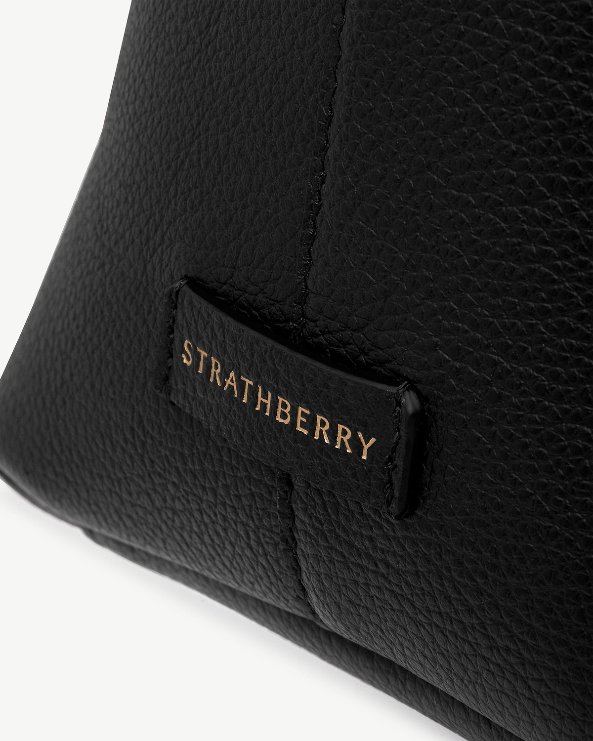 Black pebbled leather tote showing gold Strathberry logo on a leather tab