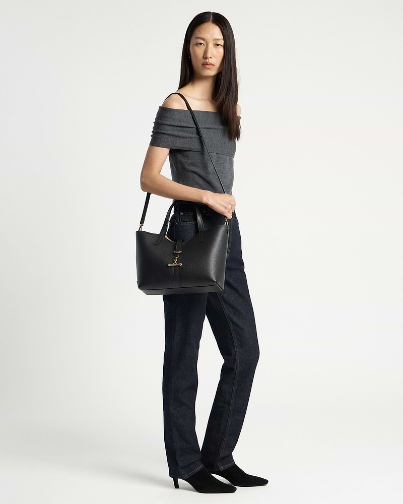 Model wearing grey off-shoulder top and dark jeans carrying black tote bag.