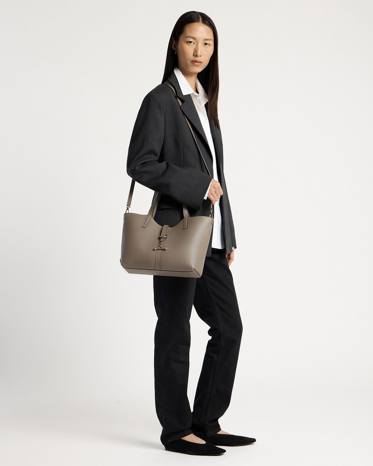 Model wearing dark blazer and white shirt, carrying a taupe tote bag on her shoulder.