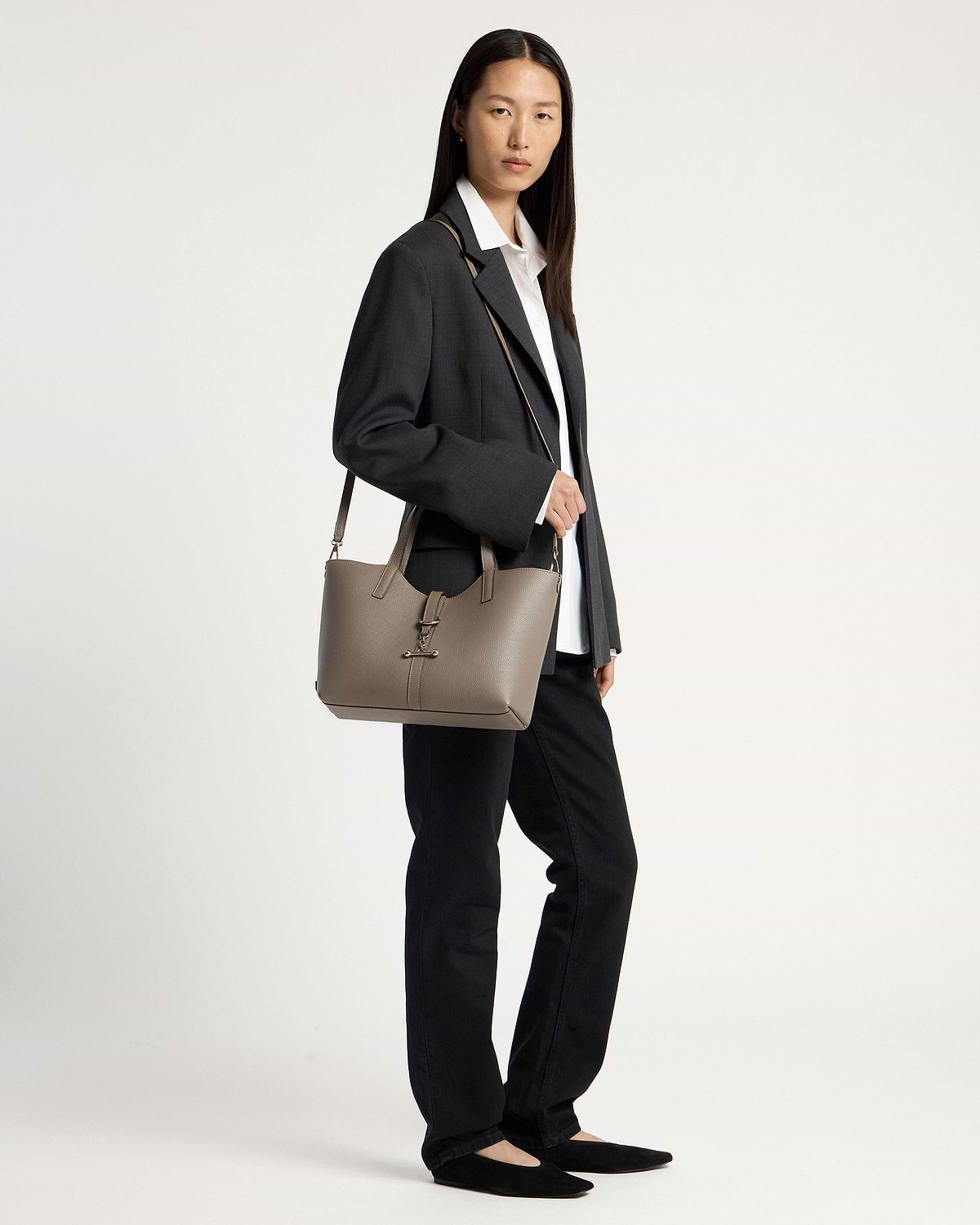 Model wearing dark blazer and white shirt, carrying a taupe tote bag on her shoulder.