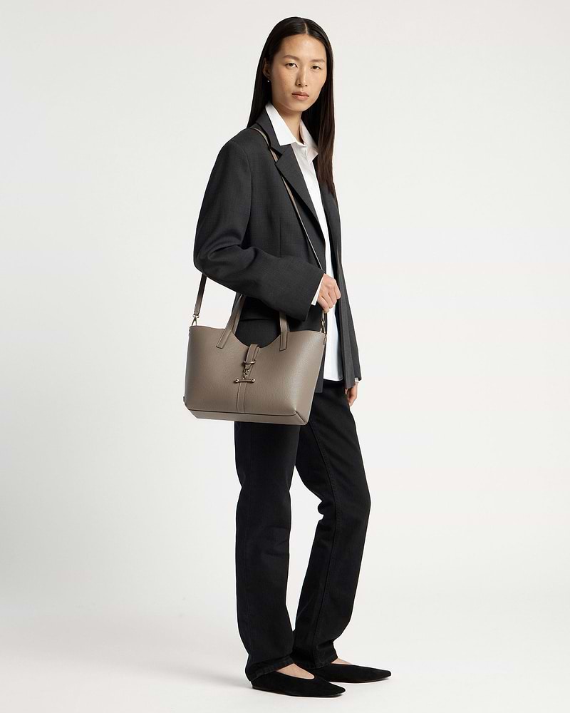 Model wearing dark blazer and white shirt, carrying a taupe tote bag on her shoulder.