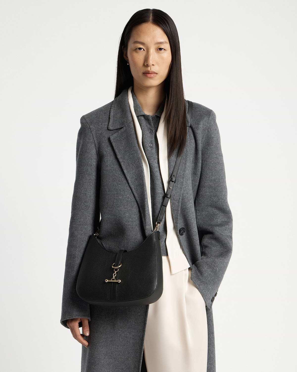 Woman in grey coat wearing black kite sling bag with gold bar fastening.