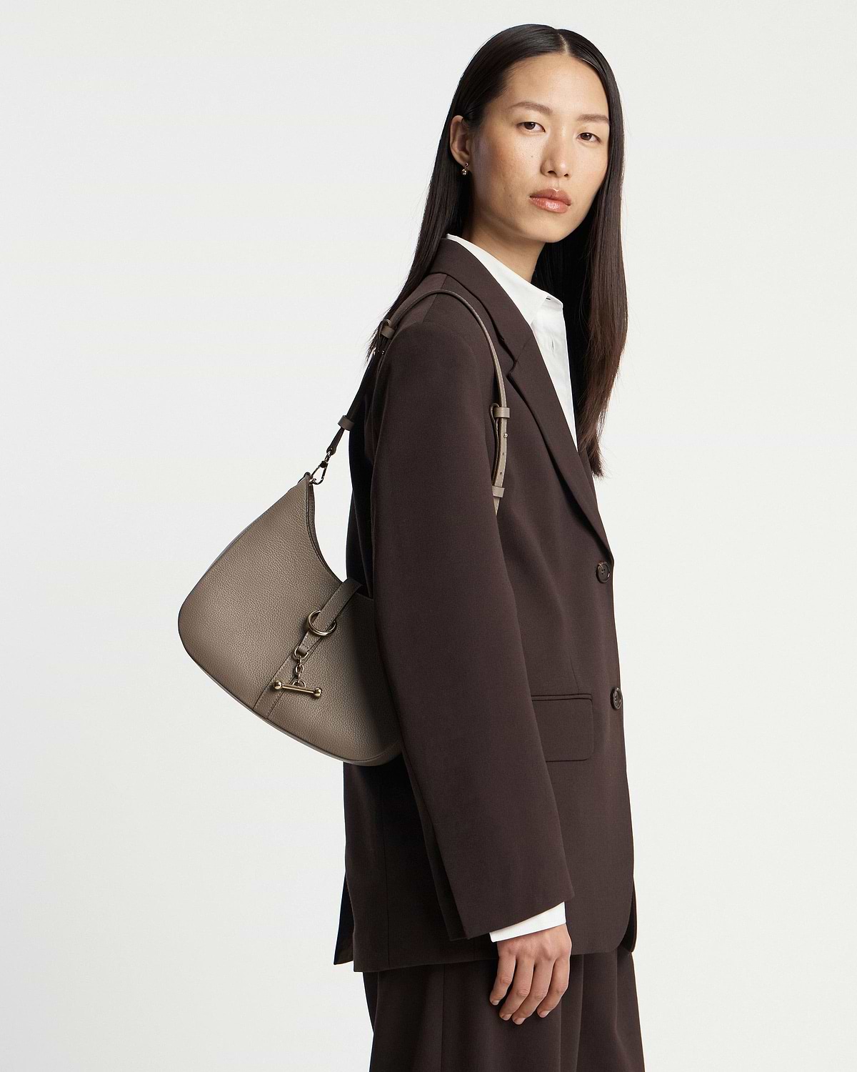 Model wearing a taupe Kite Sling bag over a dark brown blazer.
